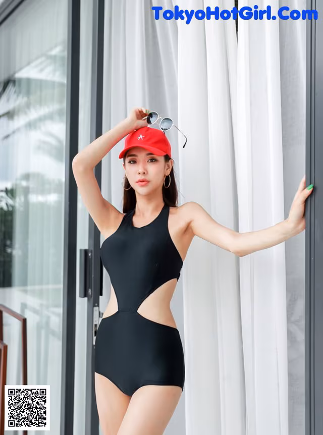 A woman in a black one piece swimsuit leaning against a window.