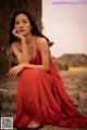 A woman in a red dress sitting on a stone wall.