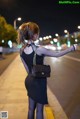 A woman in a black dress is walking down the street at night.