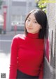 A woman in a red turtle neck sweater leaning against a wall.