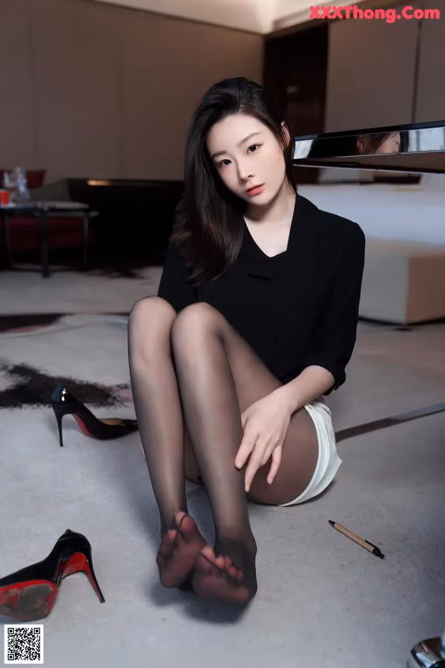 A woman sitting on the floor next to a pair of high heels.