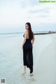 A woman in a black dress standing on a beach.