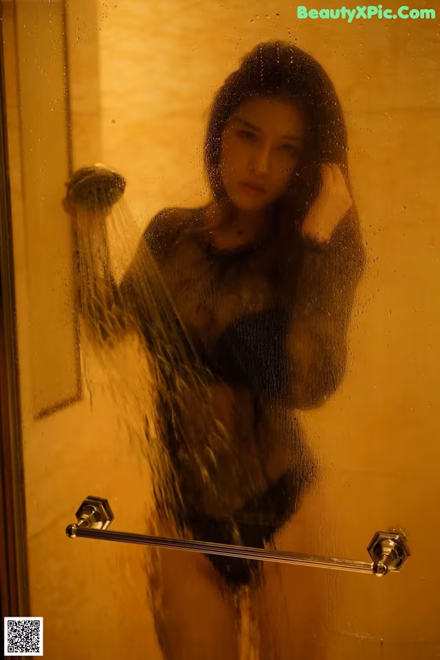 A woman standing in a shower next to a glass door.