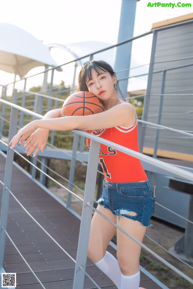 A woman in a red shirt and blue shorts holding a basketball.