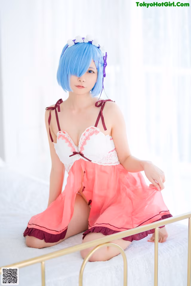A woman in a pink and white dress sitting on a bed.