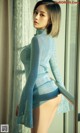 A woman in a blue sweater is posing by a window.