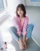 A woman in a pink shirt and jeans sitting on the floor.