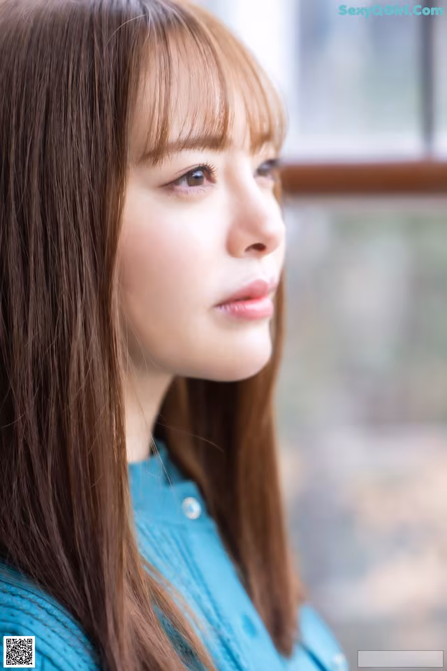 A woman with long brown hair wearing a blue sweater.