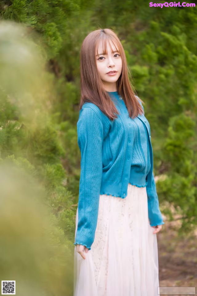 A woman in a blue sweater and a white skirt posing for a picture.