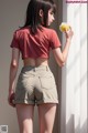 A woman in a red crop top and khaki shorts holding an apple.