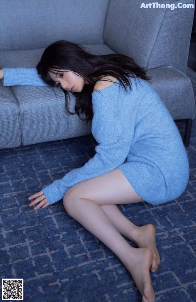 A woman in a blue sweater is sitting on the floor.