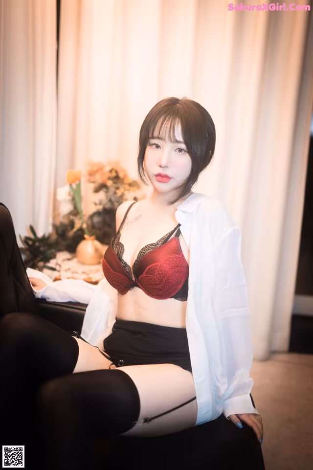 A woman sitting on a chair wearing a red bra and black skirt.