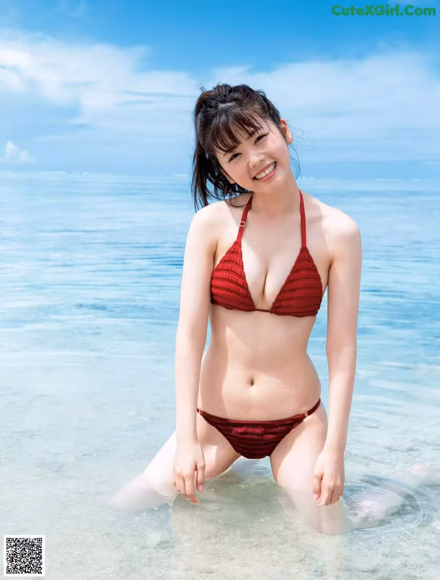 A woman in a red bikini sitting in the water.