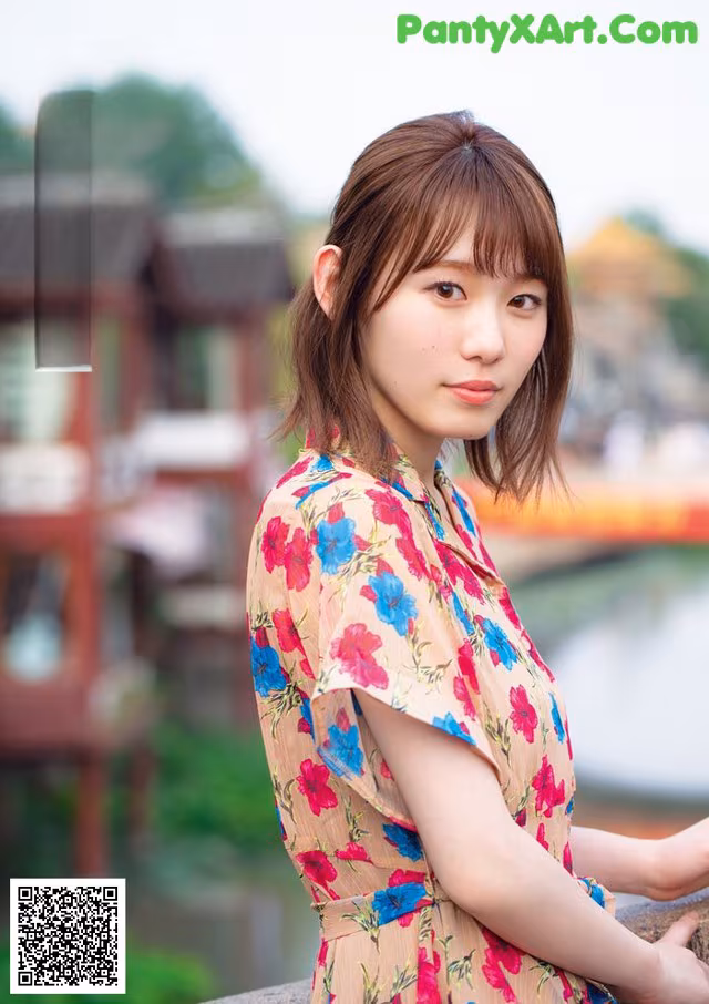 A woman in a floral dress leaning against a wall.