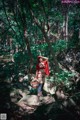 A woman in a red riding hoodie standing on a rock in the woods.